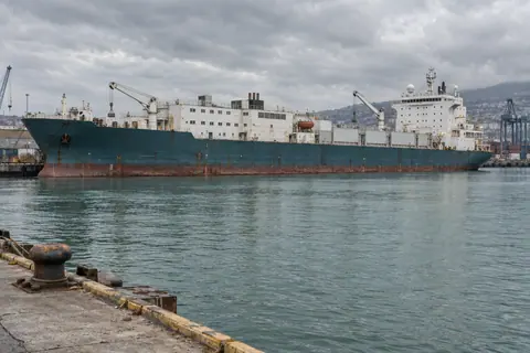 AI-generated illustration: A large unmarked factory ship moored in an industrial port.