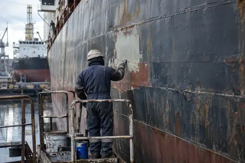 AI-generated illustration: A shipyard worker preparing a patch of a cargo ship hull.