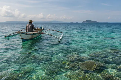 AI-generated illustration: A wooden outrigger fishing boat above shallow tropical reef water.