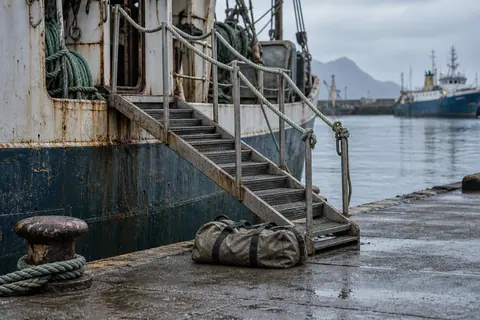 AI-generated illustration: An empty gangway between a fishing vessel and a quiet port quay.